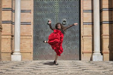 Genç, güzel, esmer, siyah gömlekli, kırmızı etekli, siyah metal bir kapının önünde flamenko dansı yapan bir kadın. Flamenko konsepti, dans, sanat, tipik İspanyolca.