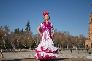 Flamenko yapan, kameraya poz veren, Sevilla 'da güzel bir meydandaki köprüde tipik flamenko elbisesi giyen bir kız. Dans konsepti, flamenko, tipik İspanyolca, Sevilla, İspanya.