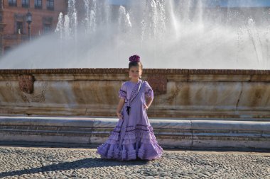 Flamenko yapan, kameraya poz veren kız Sevilla 'daki güzel bir meydanda fıskiyenin yanında tipik flamenko kostümü giyiyor. Dans konsepti, flamenko, tipik İspanyolca, Sevilla, İspanya.