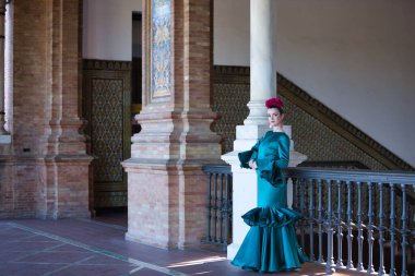 Genç, güzel, sarışın, tipik yeşil renkli flamenko takım elbiseli, demir parmaklıkların yanında poz veriyor. Flamenko konsepti, tipik İspanyolca, Sevilla, Endülüs.