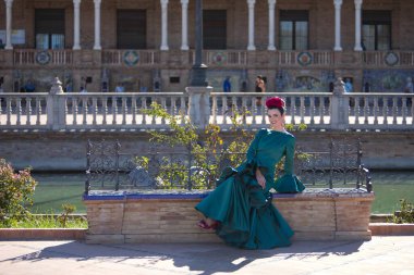 Tipik yeşil renkli flamenko takım elbiseli genç, güzel, sarışın bir kadın fayanslı ve tuğladan bir bankta poz veriyor. Flamenko konsepti, tipik İspanyolca, Sevilla, Endülüs.
