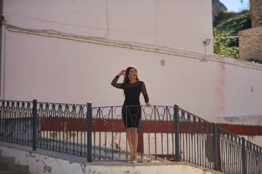 Genç, güzel, esmer, zarif siyah elbiseli, saçlarına dokunan, güzel beyaz bir Endülüs köyünde korkuluklara yaslanmış dikkati dağılmış genç bir kadın. Güzelliği, modayı, trendi, seyahati kavra.