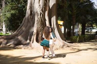 Latin kadınlar, genç, arka planda büyük bir ağaç olan arka planda dans eden bir çift, farklı dans figürleri sergiliyorlar. Konsept danslar, şehir dansları, Latince.