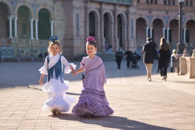 Sevilla 'da güzel bir meydanda tipik bir flamenko elbiseyle yürüyen ve mutlu bir şekilde konuşan iki kız. Dans konsepti, flamenko, tipik İspanyolca, Sevilla, İspanya.