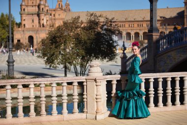 Tipik yeşil flamenko takım elbiseli, taş korkuluklara yaslanmış genç, güzel, sarışın bir kadın. Flamenko konsepti, tipik İspanyolca, Sevilla, Endülüs.