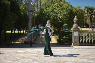 Yeşil parti elbisesi içinde genç, güzel, sarışın bir kadın pullu, pırlanta bir taç ve güzellik yarışması kazananı kuşağı ile hava pelerinini havaya uçuracak şekilde dönüyor. Güzellik kavramı, moda, gösteri.