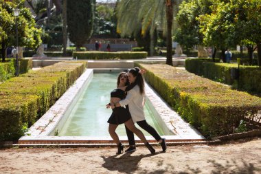 Birkaç Latin kadın, genç, arka planda fıskiyesi olan güzel bir fıskiyeyle dans eden, farklı dans figürleri sergileyen. Konsept danslar, şehir dansları, Latince.