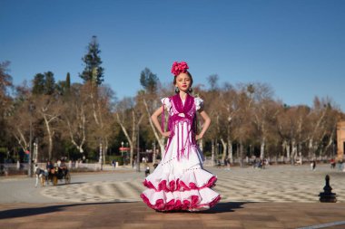 Flamenko yapan, kameraya poz veren, Sevilla 'da güzel bir meydandaki köprüde tipik flamenko elbisesi giyen bir kız. Dans konsepti, flamenko, tipik İspanyolca, Sevilla, İspanya.