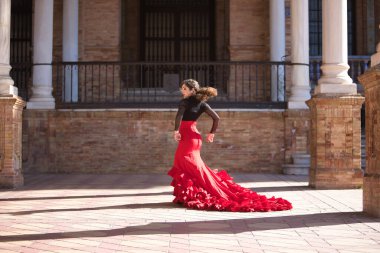 Genç, güzel, esmer, siyah gömlekli, kırmızı etekli, İspanya meydanında mermer sütunlar arasında flamenko dansı yapan bir kadın. Flamenko konsepti, dans, sanat, tipik İspanyolca.