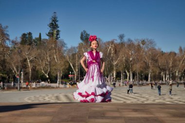 Flamenko yapan, kameraya poz veren, Sevilla 'da güzel bir meydandaki köprüde tipik flamenko elbisesi giyen bir kız. Dans konsepti, flamenko, tipik İspanyolca, Sevilla, İspanya.