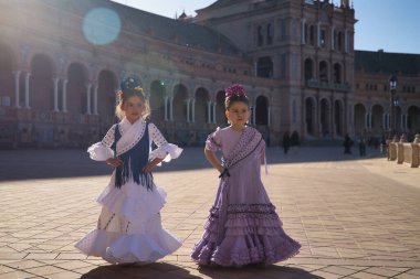 İki kız flamenko yapıyor, dikkatleri dağınık görünüyor, Sevilla 'da güzel bir meydanda tipik flamenko elbiseler giyiyorlar. Dans konsepti, flamenko, tipik İspanyolca, Sevilla, İspanya.