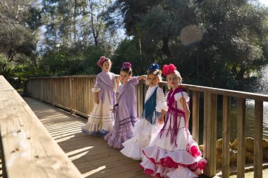 Flamenko yapan dört kız, kameraya bakarak poz veriyorlar, tipik flamenko elbiseler içinde, tahta bir köprüde. Konsept dansı, flamenko, tipik İspanyolca, Sevilla, İspanya.