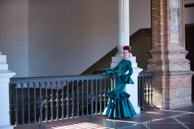 Genç, güzel, sarışın, tipik yeşil renkli flamenko takım elbiseli, demir parmaklıkların yanında poz veriyor. Flamenko konsepti, tipik İspanyolca, Sevilla, Endülüs.