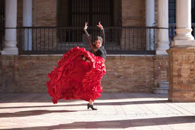 Genç, güzel, esmer, siyah gömlekli, kırmızı etekli, İspanya meydanında mermer sütunlar arasında flamenko dansı yapan bir kadın. Flamenko konsepti, dans, sanat, tipik İspanyolca.
