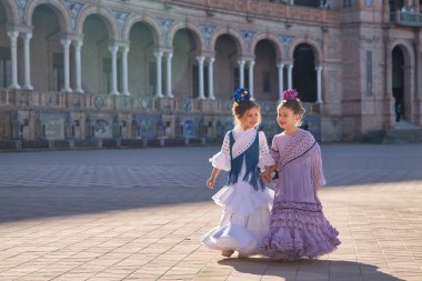 Sevilla 'da güzel bir meydanda tipik bir flamenko elbiseyle yürüyen ve mutlu bir şekilde konuşan iki kız. Dans konsepti, flamenko, tipik İspanyolca, Sevilla, İspanya.
