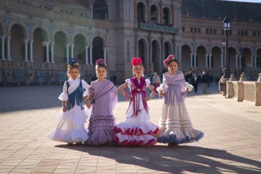 Flamenko yapan dört kız, kameraya bakarak poz veriyorlar, Sevilla 'da güzel bir meydanda tipik flamenko elbiseler giyiyorlar. Dans konsepti, flamenko, tipik İspanyolca, Sevilla, İspanya.