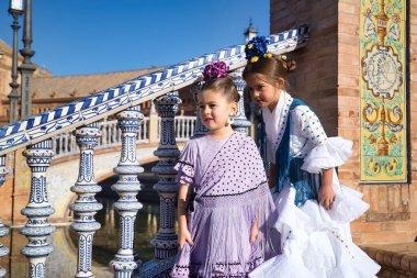 İki kız flamenko dansı yaparken, biri diğerinin kulağına konuşuyor, tipik flamenko kostümleriyle Seville 'deki güzel bir meydanda merdivenlerde. Dans konsepti, flamenko, tipik İspanyol, İspanya.