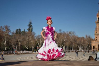 Flamenko yapan, kameraya poz veren, Sevilla 'da güzel bir meydandaki köprüde tipik flamenko elbisesi giyen bir kız. Dans konsepti, flamenko, tipik İspanyolca, Sevilla, İspanya.