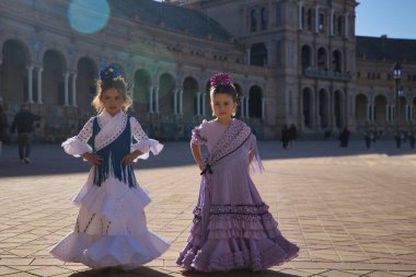 İki kız flamenko yapıyor, dikkatleri dağınık görünüyor, Sevilla 'da güzel bir meydanda tipik flamenko elbiseler giyiyorlar. Dans konsepti, flamenko, tipik İspanyolca, Sevilla, İspanya.
