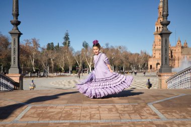 Kız flamenko yapıyor, kostümünü göstermek için kıvırıyor Sevilla 'da güzel bir meydanda, köprüde tipik bir flamenko elbisesi giyiyor. Dans konsepti, flamenko, tipik İspanyolca, Sevilla, İspanya.