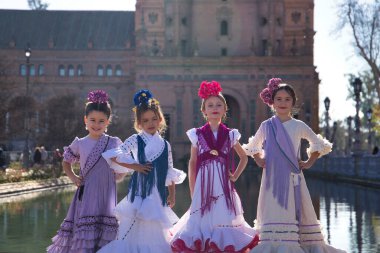 Flamenko yapan dört kız, kameraya bakarak poz veriyorlar, tipik flamenko kostümleriyle Sevilla 'da güzel bir meydanda gölün yanında. Konsept dansı, flamenko, tipik İspanyolca, Sevilla, İspanya.
