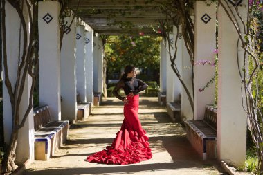 Genç, güzel, esmer, siyah gömlekli, kırmızı etekli, parkta beyaz sütunların ortasında flamenko dansı yapan bir kadın. Flamenko konsepti, dans, sanat, tipik İspanyolca.