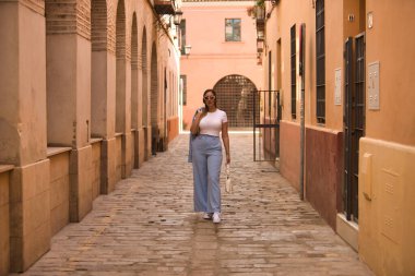 Kahverengi saçlı, güneş gözlüklü, mavi ceketli yalnız bir sokakta omzunun üstünde ceketiyle yürüyen güzel bir kadın. Güzelliği, modayı, eğilimi kavra.