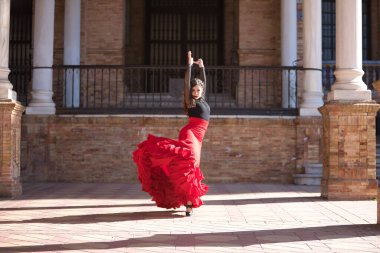 Genç, güzel, esmer, siyah gömlekli, kırmızı etekli, İspanya meydanında mermer sütunlar arasında flamenko dansı yapan bir kadın. Flamenko konsepti, dans, sanat, tipik İspanyolca.