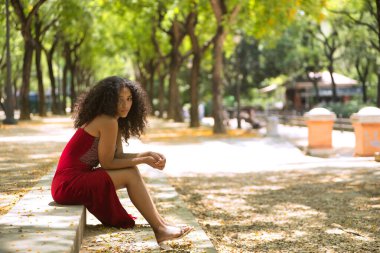 Genç bir kadın, güzel, Latin, kıvırcık saçlı, kırmızı elbiseli, üzgün ve melankolik bakışlı, parkın merdivenlerinde oturan. Kavram, güzellik, melankoli, üzüntü..