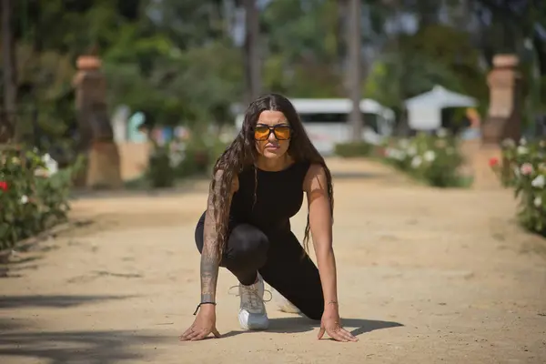 stock image Young woman, brunette, beautiful, very tattooed, with black jumpsuit and glasses with orange lenses, in position to go for a run insinuating a new beginning and female entrepreneurship.