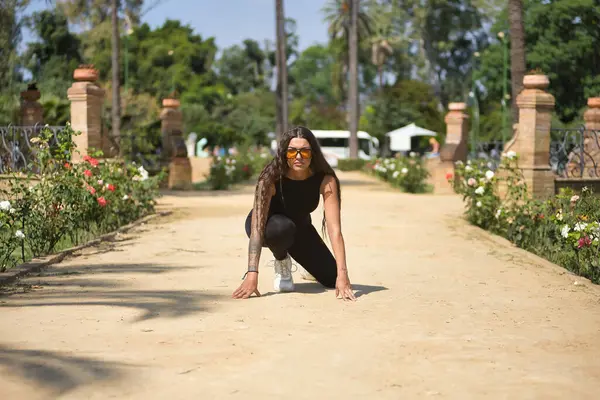 Stock image Young woman, brunette, beautiful, very tattooed, with black jumpsuit and glasses with orange lenses, in position to go for a run insinuating a new beginning and female entrepreneurship.