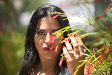 Genç, güzel, esmer, beyaz elbiseli Latin bir kadının portresi, bir bitkinin yapraklarının ve çiçeklerinin arasından bakıyor. Güzelliği, modayı, trendi, çiçekleri, ilkbaharı kavra.