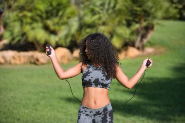 Latin kadın, genç, güzel, esmer, kıvırcık saçlı ve spor elbiseli ip atlamak için poz veren. Konsept spor, egzersiz, koşu, aktif.