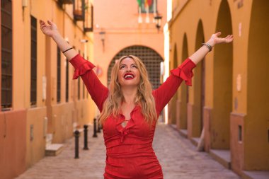 Genç bir kadın, güzel, sarışın, kırmızı elbiseli, kolları havada, mutlu, memnun ve Tanrı 'ya ve hayata minnettar. Minnettarlık, mutluluk, neşe, din kavramını.