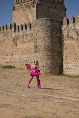 Sürüklenen kraliçe, sarışın, çekici, tacıyla, elbisesiyle, yüksek topuklu botlarıyla ve pembe yelpazesiyle arka planda bir şatoyla dışarı çıkıyor. Gurur, kimlik, sanatçı kavramı. Dikey konum.