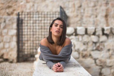 Genç, güzel, esmer, İspanyol bir kadının portresi, gri bir elbise giymiş, üzgün ve şefkatli bir bakışla, taş bir duvarda yatıyor. Kavram moda, güzellik, moda, kadınlık.