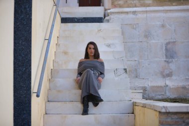 Genç, güzel, esmer, İspanyol kadın, gri bir elbise ve çizme giyiyor, kameraya bakıyor, merdivenlerde oturuyor. Kavram moda, güzellik, moda, kadınlık.