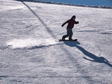 Güneşli bir kış gününde bir tatil köyünde kayak pistinde sporunu icra eden snowboardcu. Kar, spor, mevsim, kış kavramları.