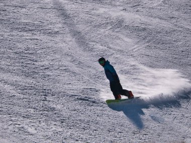 Güneşli bir kış gününde bir tatil köyünde kayak pistinde sporunu icra eden snowboardcu. Kar, spor, mevsim, kış kavramları.