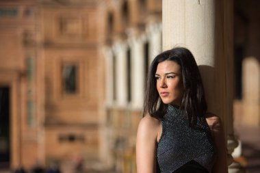 Süslü, siyah elbiseli esmer bir kadının portresi. Sevilla 'daki İspanya meydanına bakıyor ve mermer bir sütuna yaslanıyor. Güzelliği, modayı, kadınlığı, turizmi kavra.