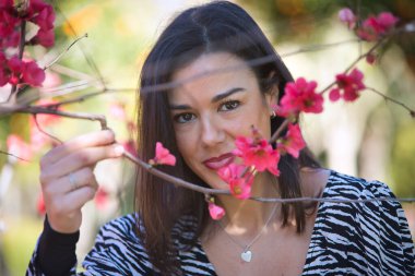 Genç, güzel, siyah saçlı, zebra elbiseli bir kadının portresi, yüzünü dallar ve Japon ayva çiçekleri ile kaplıyor. Güzelliği, modayı, eğilimi, dişiliği, doğayı, ağaçları kavra.