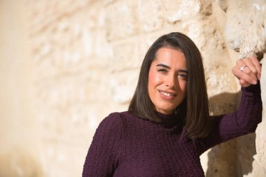 Genç, güzel, esmer, İspanyol bir kadının portresi, mor bir elbise giymiş, duvara yaslanmış, gülümseyen, mutlu ve muzaffer bir şekilde kameraya bakıyor. Güzelliği, modayı, modayı kavra.