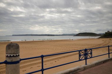 Santander 'de Sardinero plajı. Şafak vakti bulutlu bir günde. İnsanlar sahilde yürüyor ve spor yapıyor. Konsept seyahat, tatil, varış yerleri, sahil, yaz.