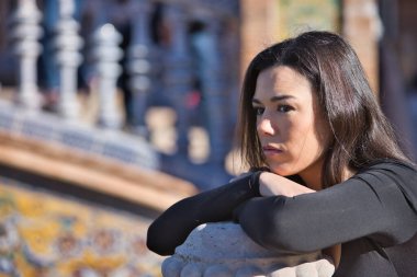 Siyah uzun kollu tişörtlü, genç, güzel, koyu renk saçlı bir kadının portresi. Dalgın ve konsantre. Elleri bir balkonun üzerinde dinleniyor. Düşleri, düşünceleri, konsantrasyonu kavra.