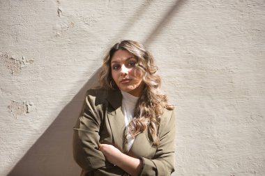 Genç, güzel, sarışın bir kadının portresi, yeşil bir ceket giyiyor, kolları çapraz, kameraya bakıyor, bağımsız ve güçlü, duvara yaslanmış..