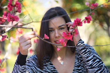 Genç, güzel, siyah saçlı, zebra elbiseli bir kadının portresi, yüzünü dallar ve Japon ayva çiçekleri ile kaplıyor. Güzelliği, modayı, eğilimi, dişiliği, doğayı, ağaçları kavra.