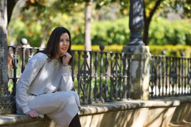 Genç, güzel, siyah saçlı, beyaz elbiseli, düşünceli ve hayalperest bir kadın, eli çenesinde, bir bankta, yalnızlık içinde oturuyor. Güzelliği, modayı, eğilimi, kadınlığı kavra.