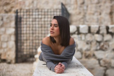 Genç, güzel, esmer, İspanyol kadın portresi, gri bir elbise giyiyor, sonsuzluğa bakıyor, taş bir duvarda yatıyor. Kavram moda, güzellik, moda, kadınlık.