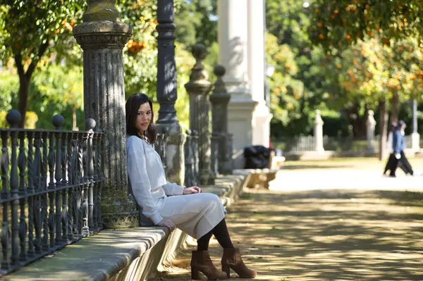 Genç, güzel, siyah saçlı, beyaz elbiseli, rahat ve sakin bir kadın, bir bankta tek başına oturuyor. Güzelliği, modayı, eğilimi, kadınlığı kavra.