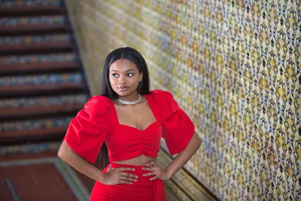 Genç, güzel, Afrikalı bir kadın, kırmızı bir elbise giyiyor, Sevilla 'da İspanya meydanının merdivenlerinde elleri belinde bir model gibi poz veriyor. Moda konsepti, güzellik, moda.